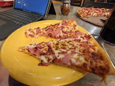 Large thin crust with extra ham, two slices on a yellow platic plate,
the rest of the pizza sitting on the board along with the serving spatula.

A laptop is hanging out to the left.

The smell of a Dr Pepper is wafting through the air.
