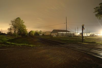 some railroad tracks in front of an industrial building at night. sorry for not describing this better. its almost 2am here.